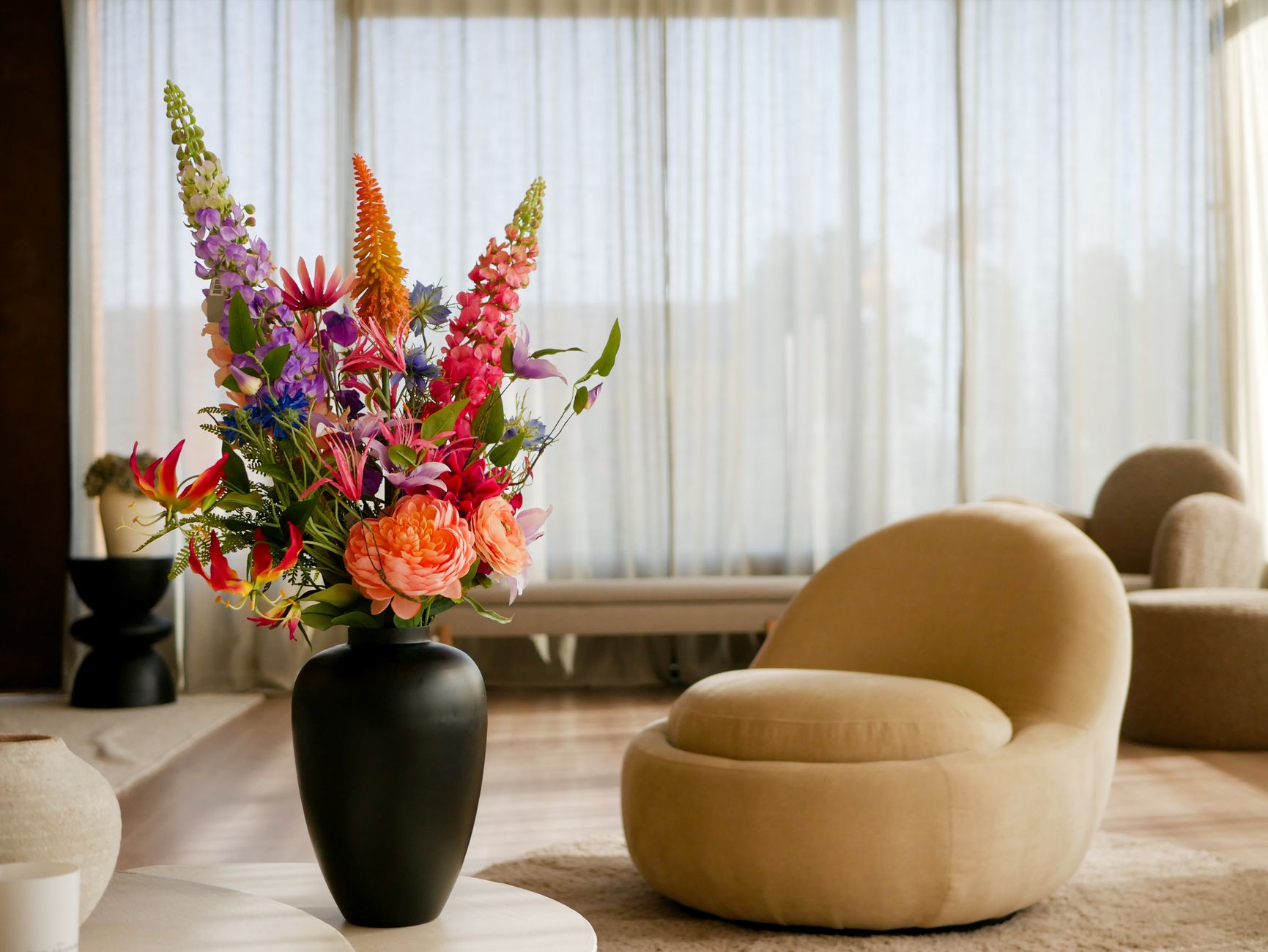 A modern living room featuring a plush beige chair and colorful flower arrangement on a table